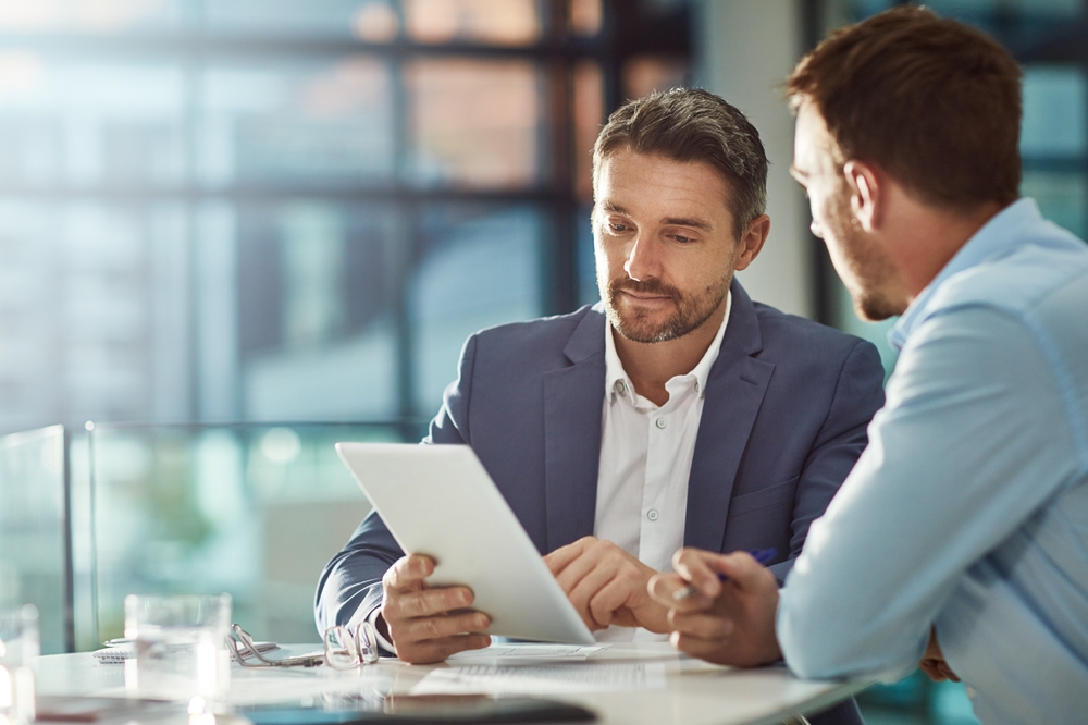 Two men reviewing content on a tablet together at an office desk