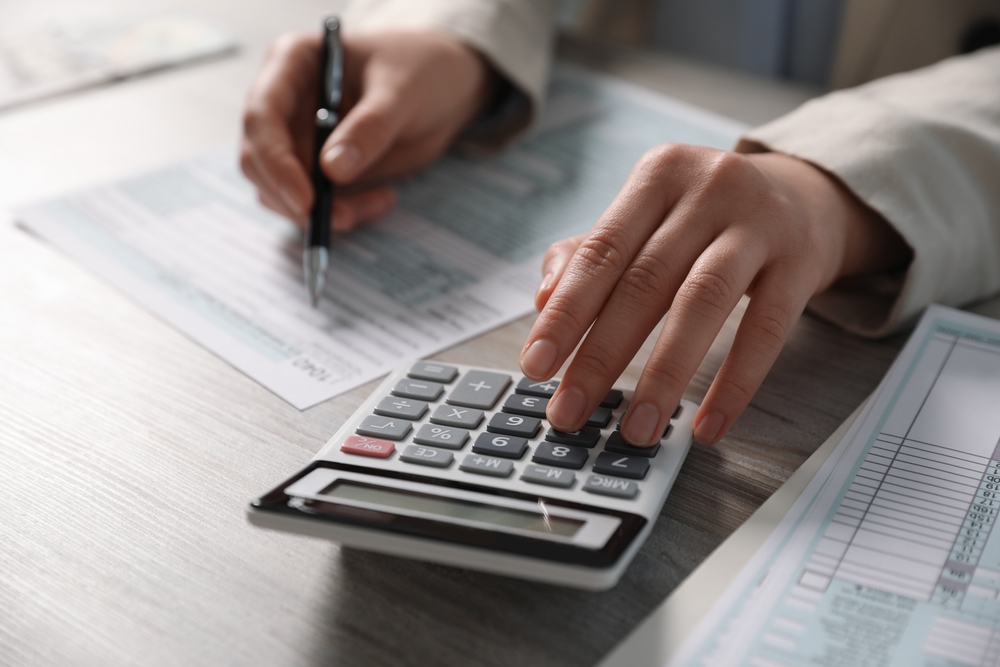 Person using a calculator and writing on paperwork at a desk