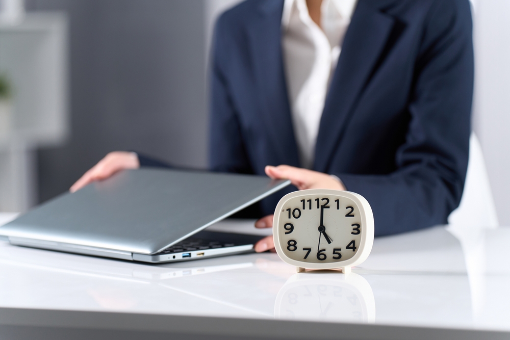 Woman closing a laptop next to a clock on a desk