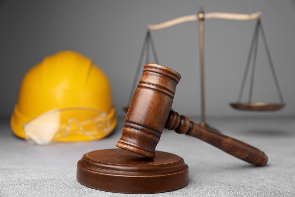 Wooden gavel and sound block beside a hard hat with safety glasses and scales of justice