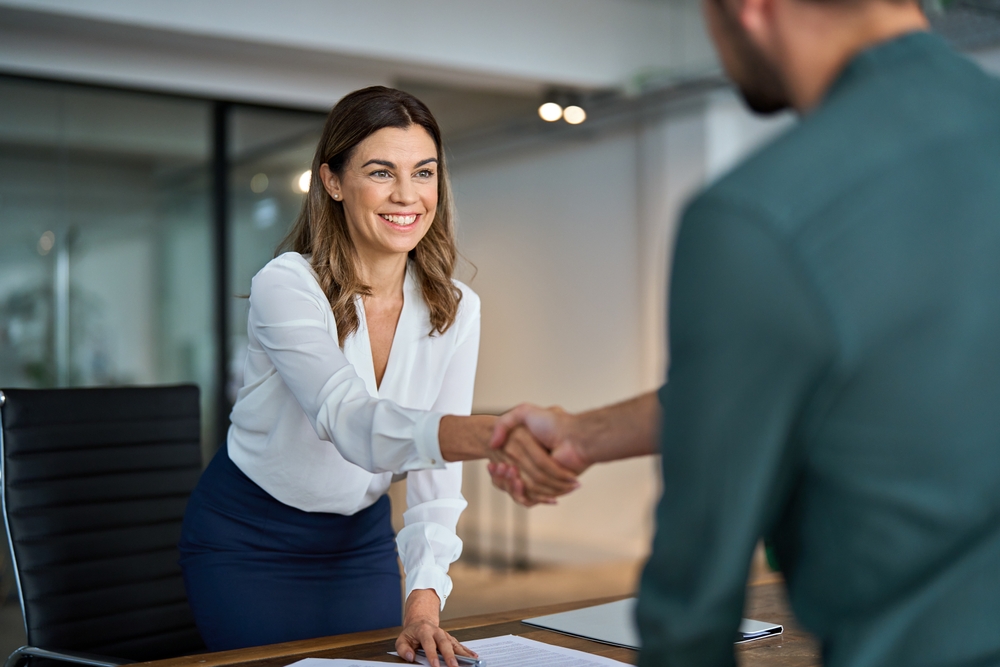 Woman shaking hands with a man across a desk in an office