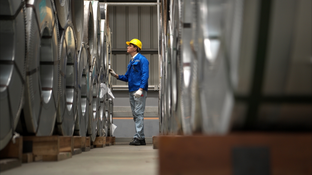 Man in a hard hat inspecting large metal coils in a warehouse