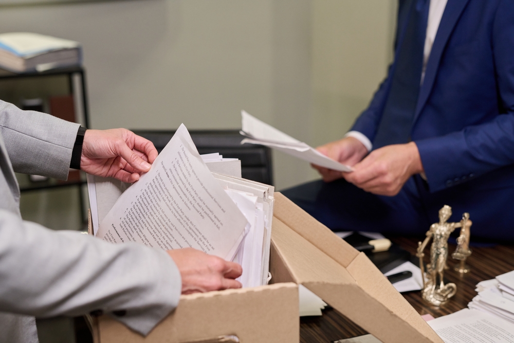 Two people going through paperwork stored in a document box, with a small statue of Lady Justice on the desk