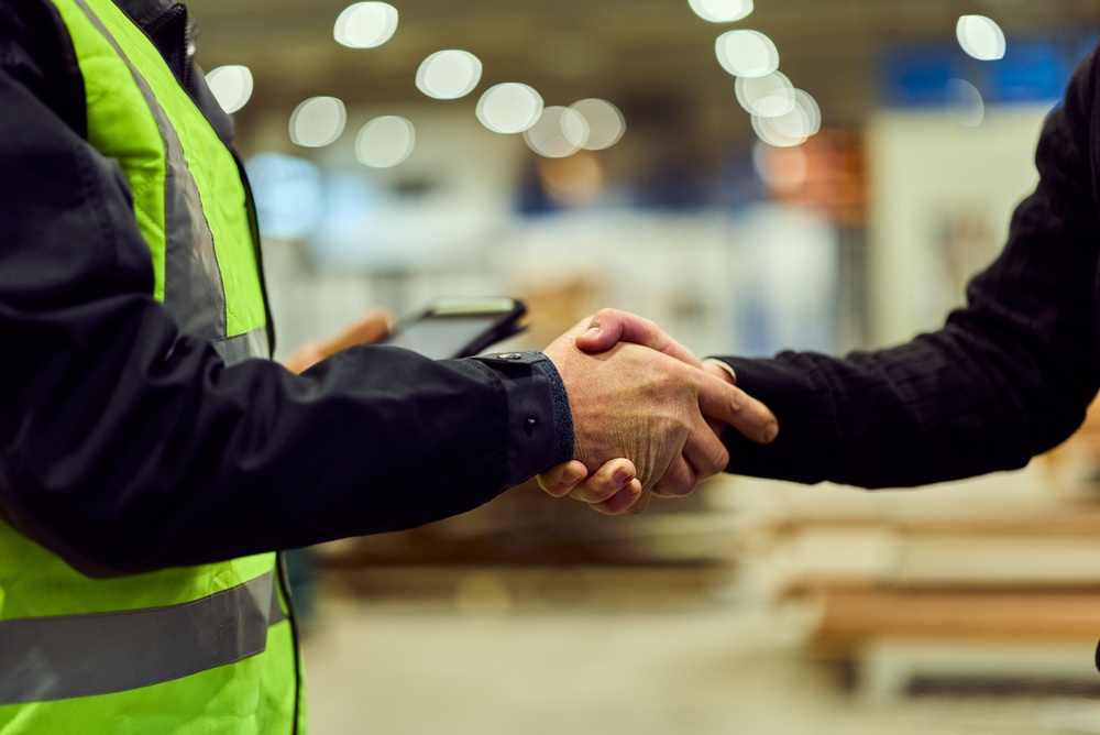 Person in a safety vest holding a tablet shaking hands with another person in a warehouse