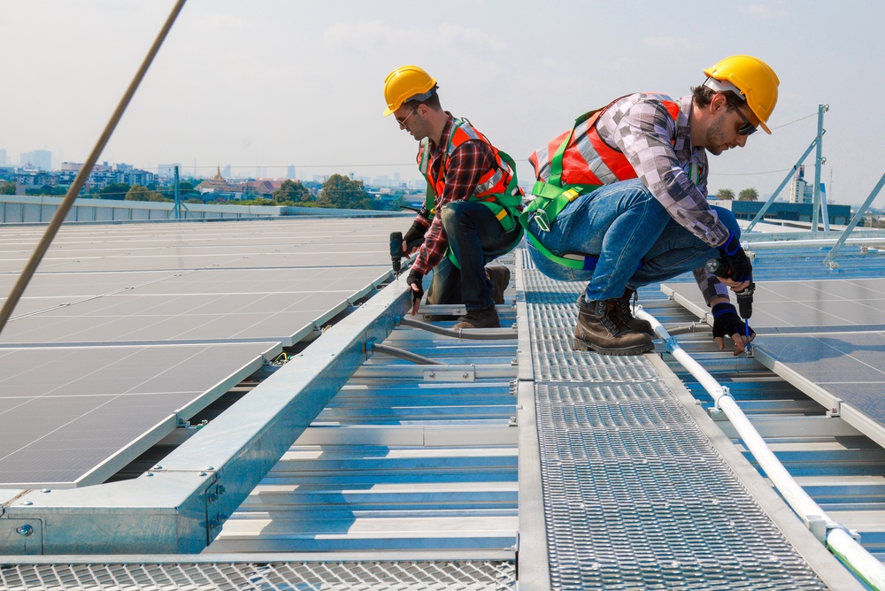 Two men wearing safety harnesses installing solar panels on a rooftop