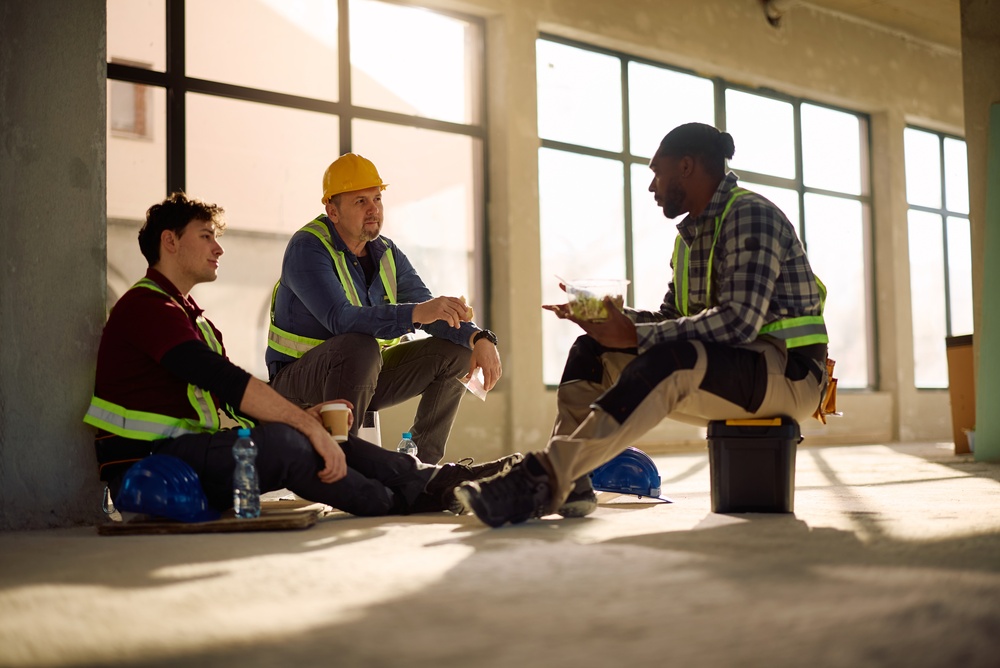 Three construction workers sitting and eating together during a break at a job site