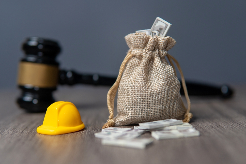 Miniature gavel, hard hat, and a money bag with stacks of cash on a table